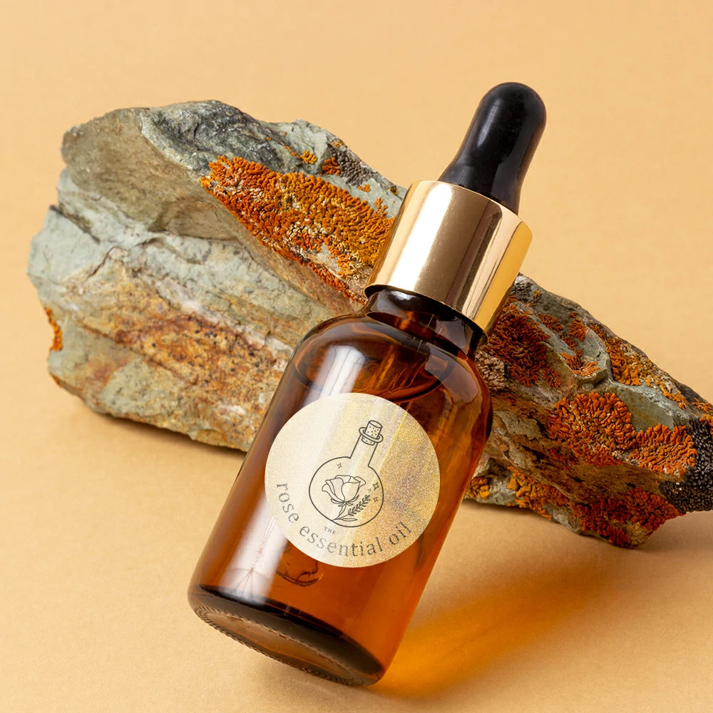Amber dropper bottle labeled rose essential oil with gold cap, displayed against a textured rock