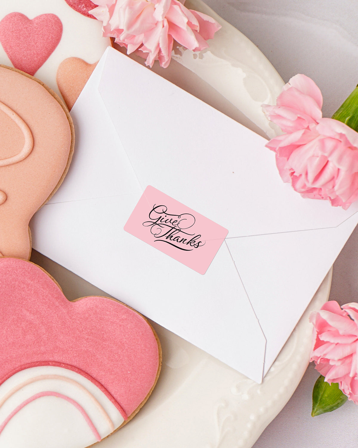 Pink thank you label on white envelope with heart cookies and pink flowers, gift packaging