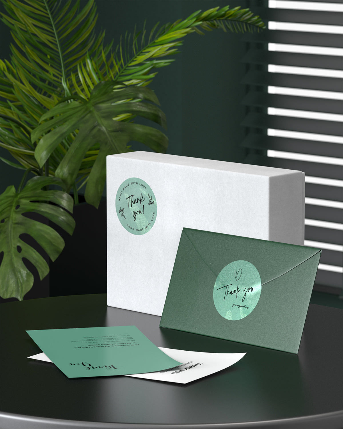 Green thank you stickers on gift box and envelope, with plants and cards in a modern setting