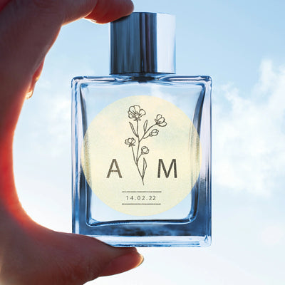 Hand holding clear glass bottle with floral thermal label, personalized monogram and date.