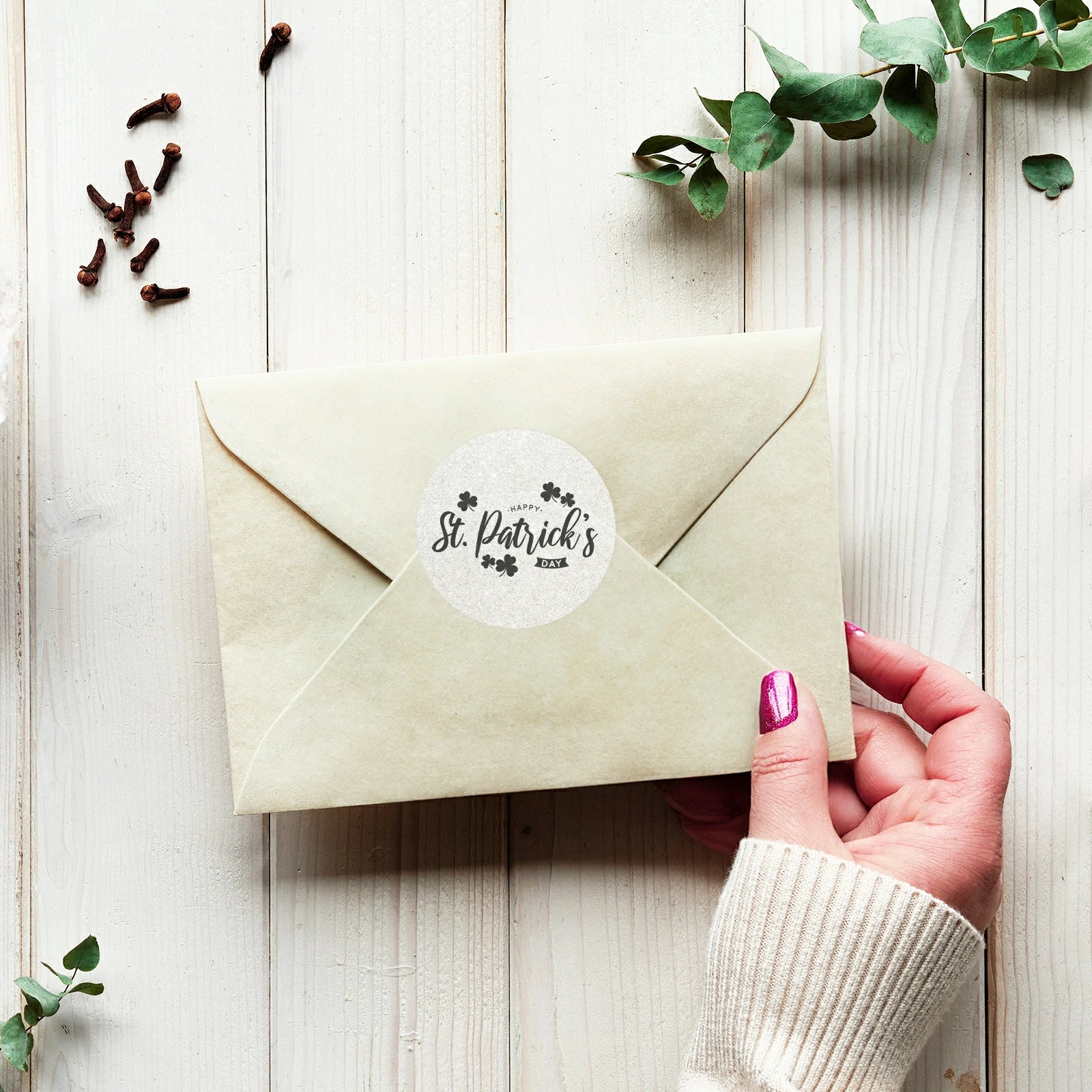 St. Patrick's Day round sticker on cream envelope held by hand on wooden table