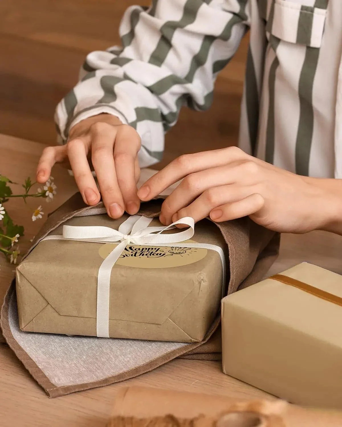 Hands wrapping birthday gift with kraft paper, ribbon, and thermal label on wooden table