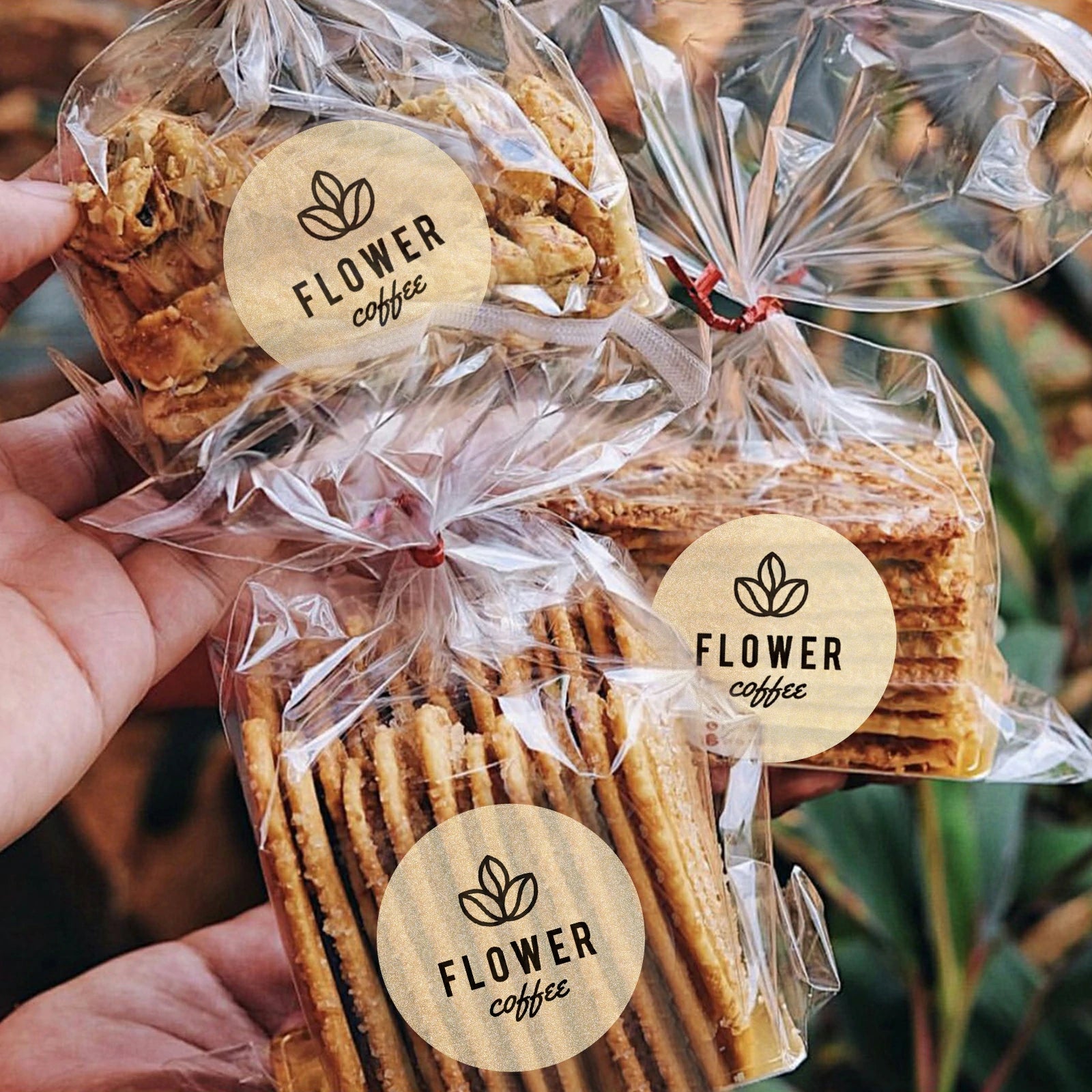 Clear plastic bags with assorted cookies labeled 'Flower coffee' held outdoors, packaged for gifting or sale.