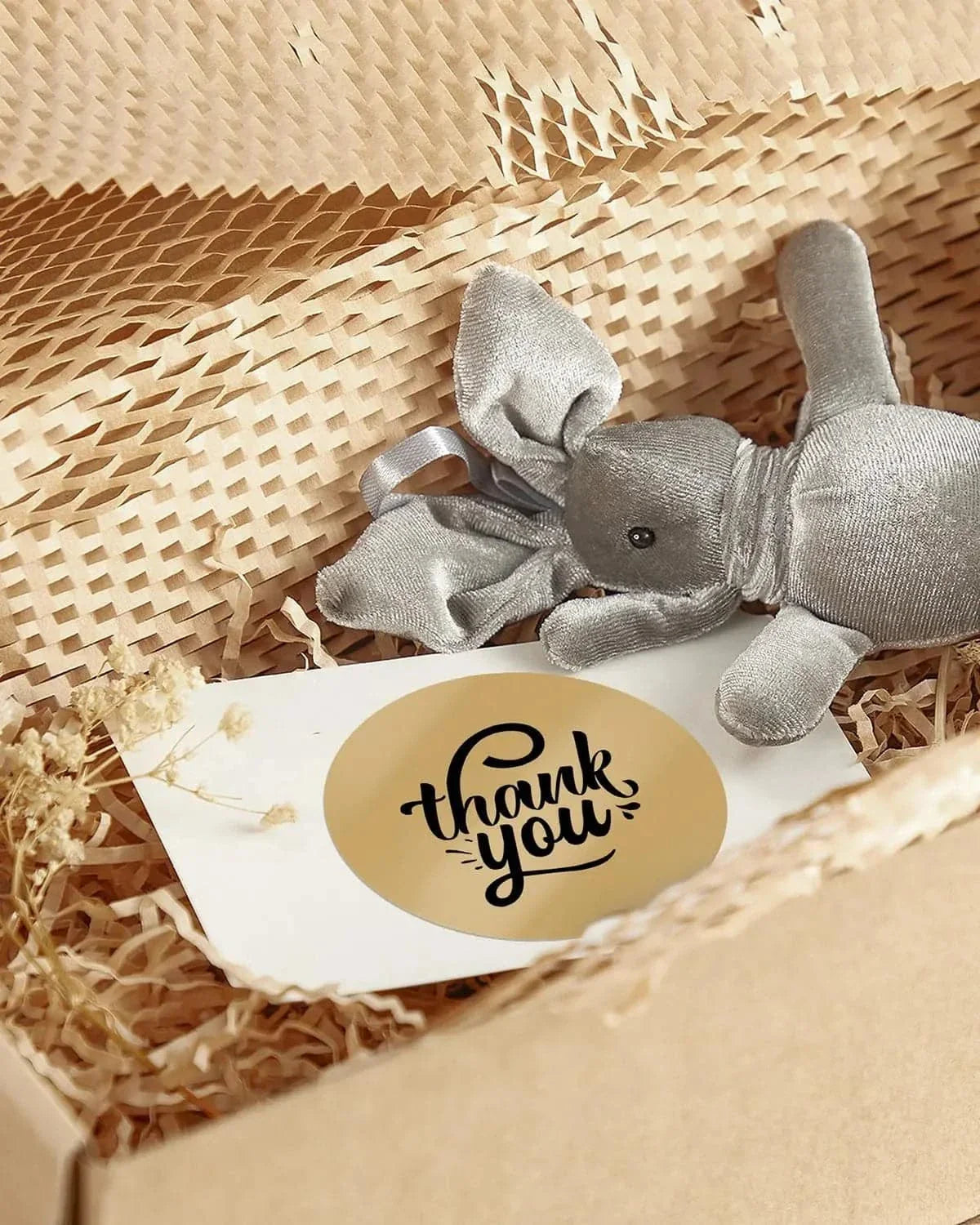 Gift box with shredded paper, thank you sticker, and grey stuffed elephant toy