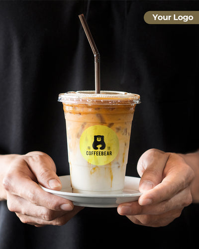 Hand holding iced coffee in a plastic cup with custom circular product label, black background