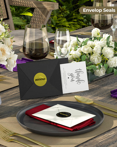 Gold glitter envelope seals on black and white invitations at an elegant table setting
