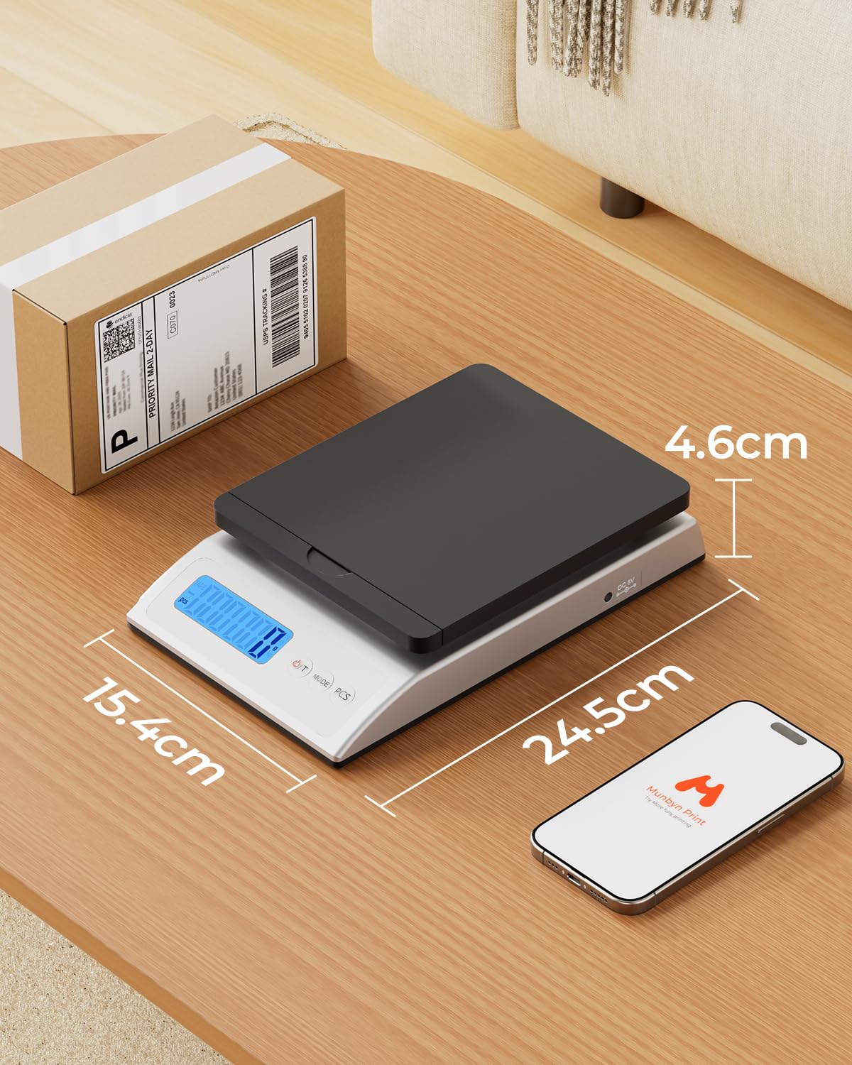 Digital shipping scale with LCD display and size dimensions, next to a labeled package and smartphone on wooden table.