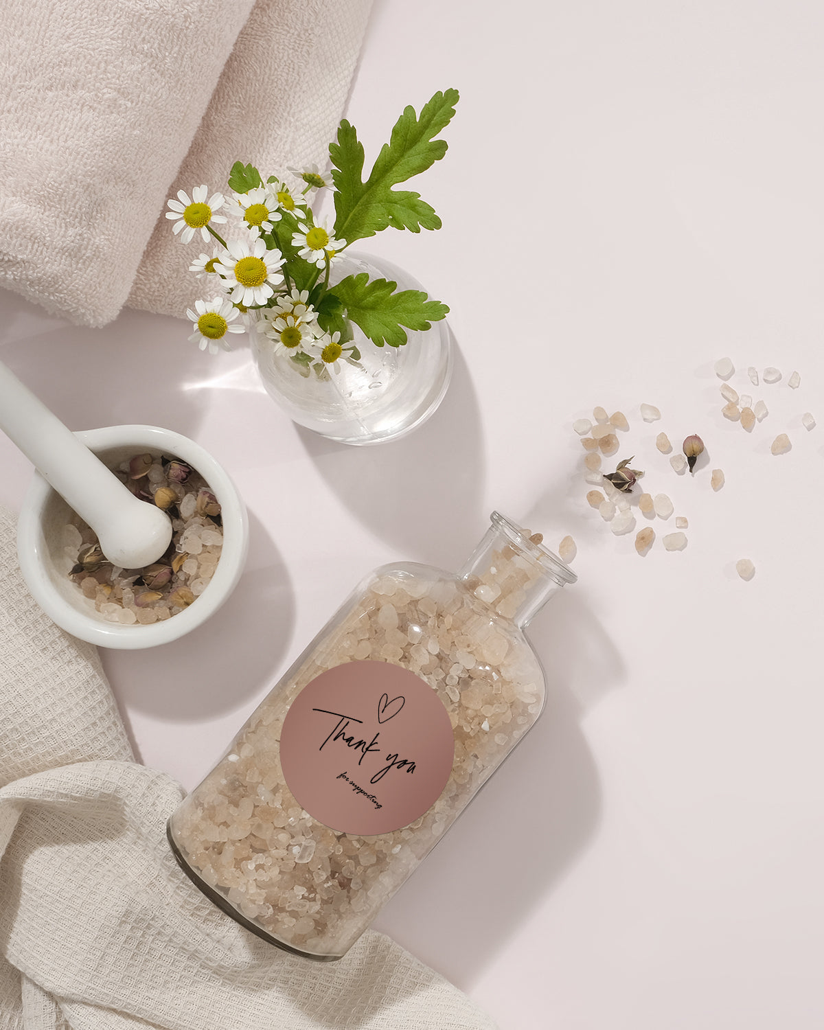 Spa flat lay with bath salts in a glass jar, chamomile flowers, towel, and mortar on soft background